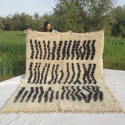 Handwoven 7x10 Beni Mrirt Moroccan rug with bold black abstract geometric patterns on white background held outdoors in grassy field