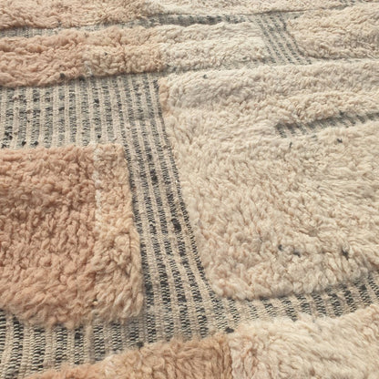 Close-up of a Beni Ourain patchwork rug showing the extraordinary softness of the natural wool pile with large blush-rose and ivory wool blocks side by side, separated by a thin grey grid - an organic, textural two-tone block composition reminiscent of abstract stone or cobblestone