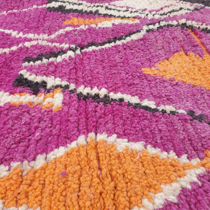 Close-up of a handwoven Boujad Berber rug showing a bold deep purple wool pile with large white cream abstract vessel and figure silhouettes and orange diamond motifs — extraordinary graphic composition with strong Amazigh symbolic roots and remarkable colour depth