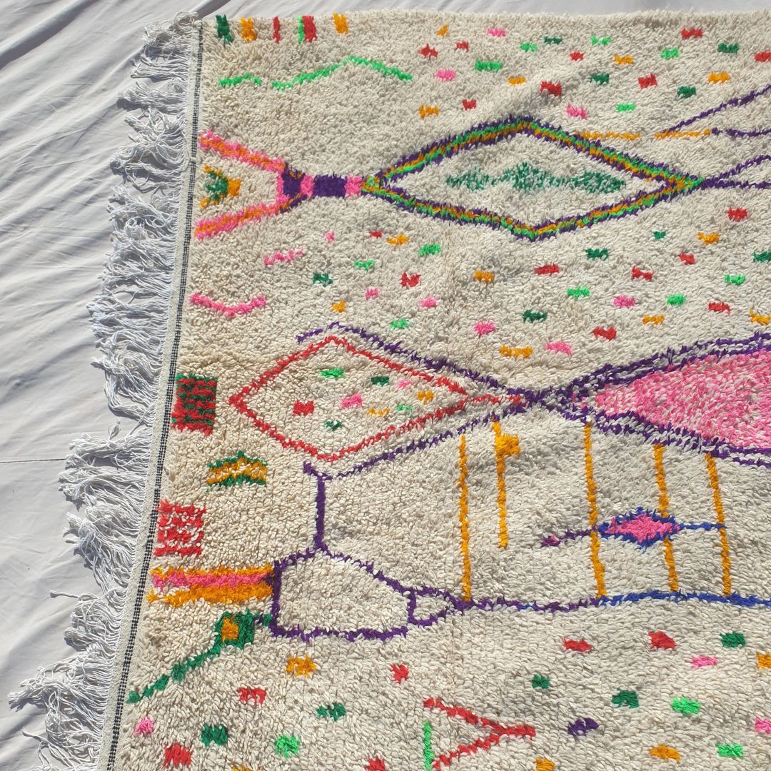 Bottom half of a white Azilal Moroccan wool rug featuring the bold navy blue and red vertical accent lines at the base, with the natural cream wool pile scattered with colorful confetti dots — showing the thick handknotted texture and natural fringe of authentic Azilal craftsmanship from Morocco's High Atlas