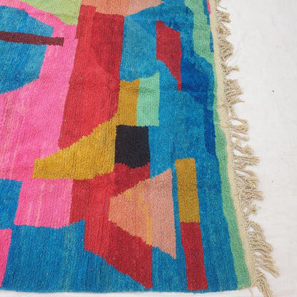 Bottom half of a large blue Moroccan wool rug with dense handknotted pile — vivid electric blue background with large bold abstract shapes in hot pink, red, yellow and green, and natural fringe at the bottom — showcasing the exceptional softness and thickness of authentic Berber wool