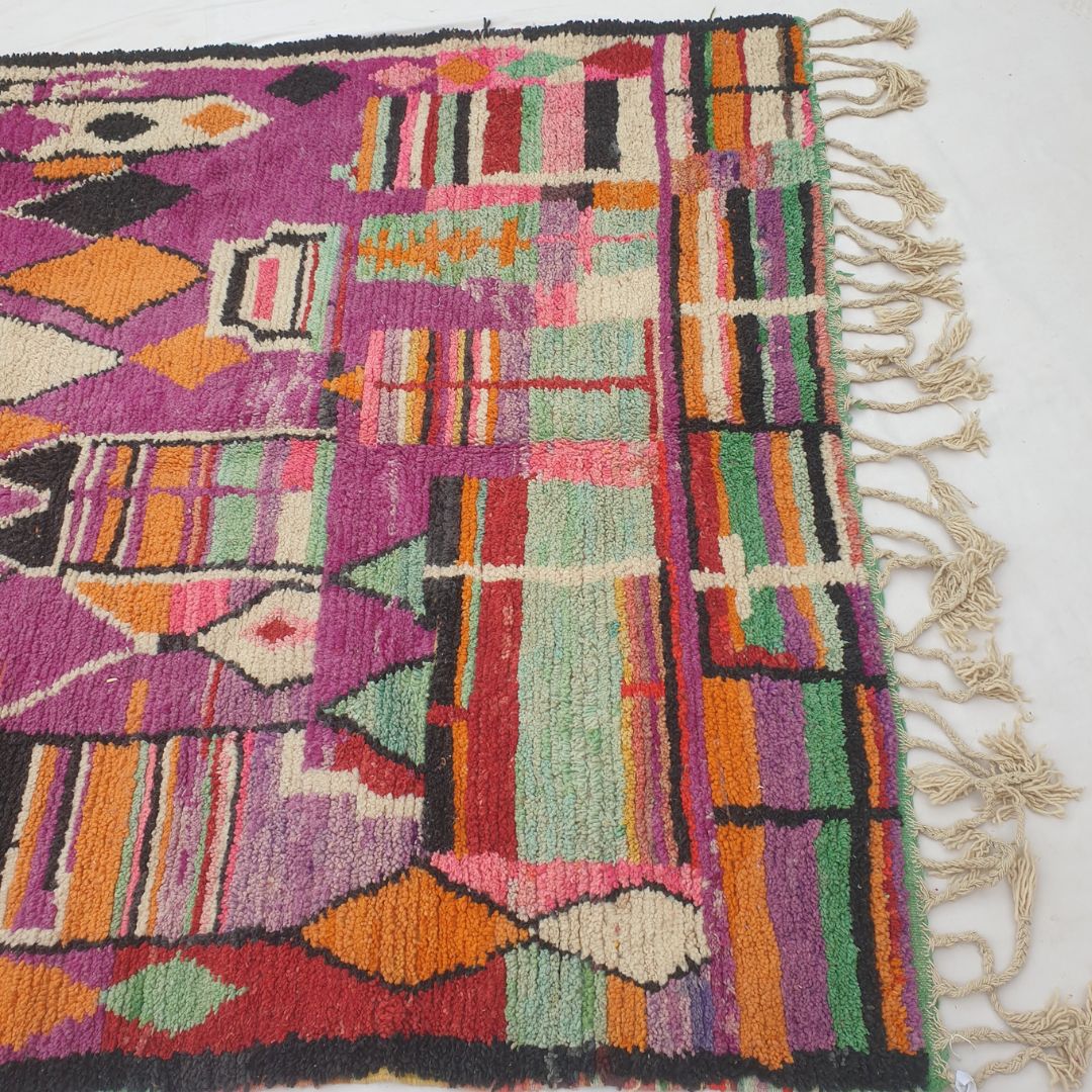 Bottom half of a deep purple Moroccan wool rug featuring a dense multicolor horizontal stripe band in green, orange, pink, black and white at the base, with a row of orange and black diamonds above — thick handknotted natural wool pile with natural fringe showing exceptional softness