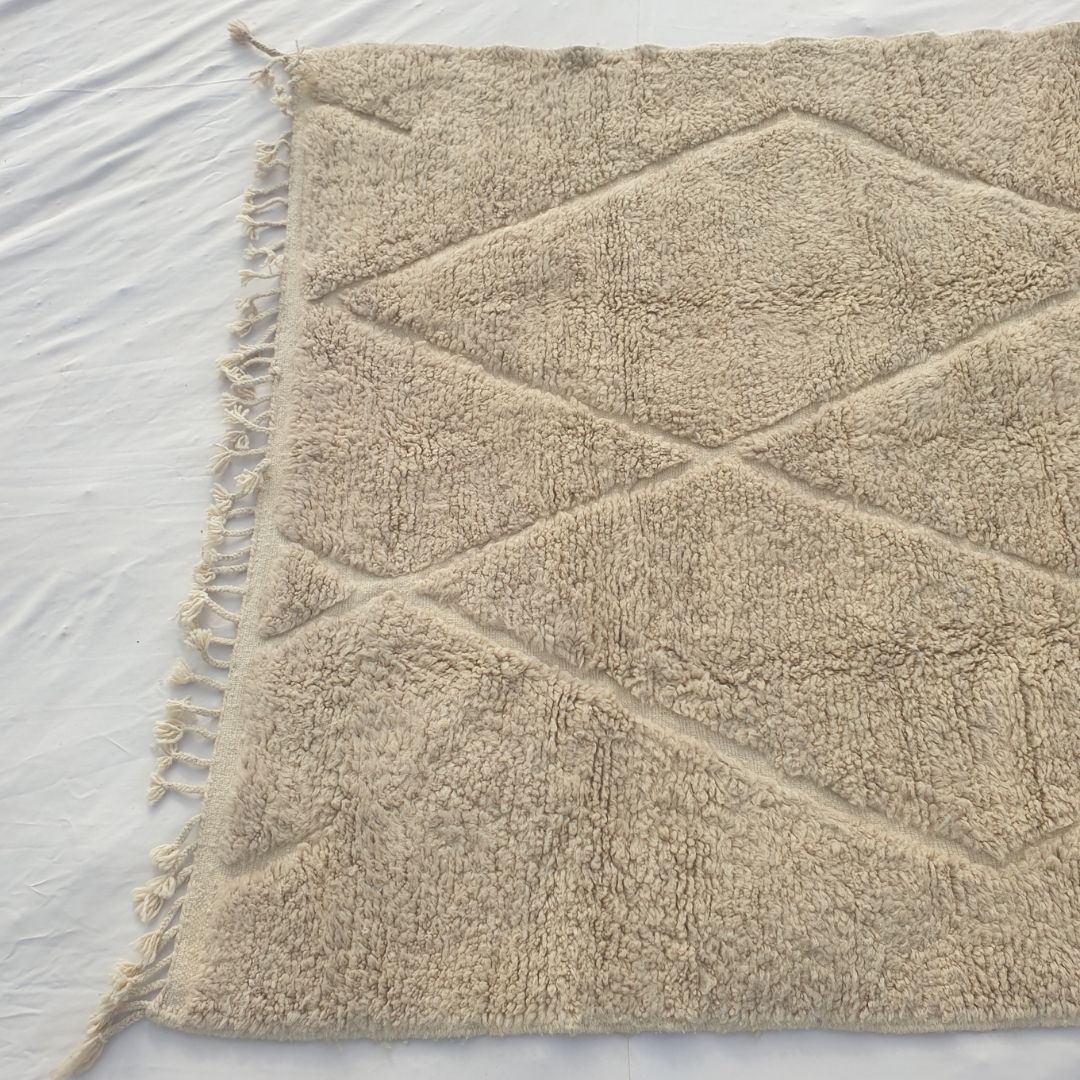 Detail shot of the ivory beige Beni Ourain diamond trellis pattern on Chaika - the carved relief lattice of crossing lines forming overlapping lozenge shapes across the warm ivory wool pile, created entirely without dye through skilled pile height variation, tone-on-tone artistry