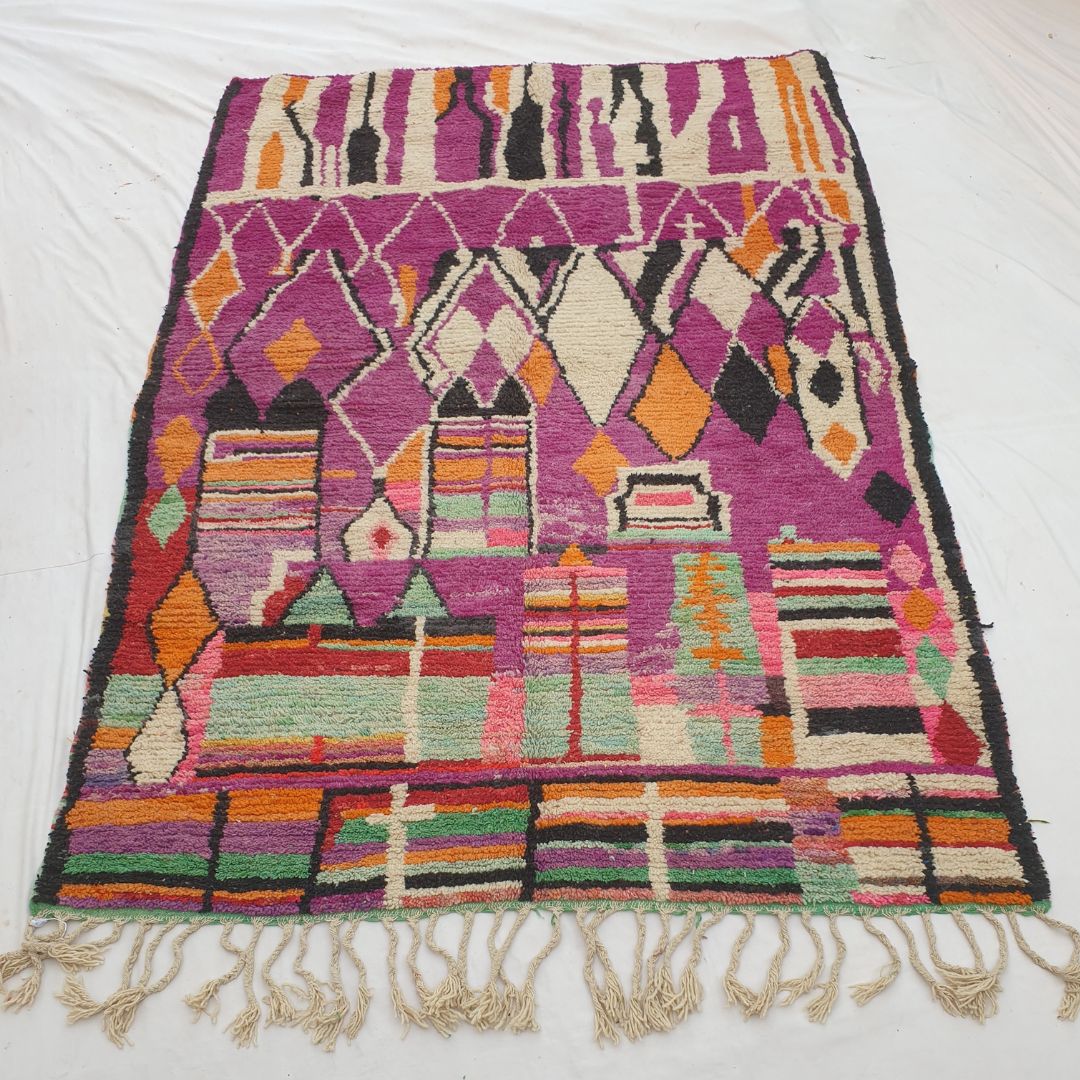 Authentic Boujad Moroccan rug 227×323 cm laid flat — deep violet purple background with large white abstract silhouette shapes in the upper zone, orange and black diamond row in the middle, and vivid multicolor stripes at the bottom, handmade in Morocco by Berber women