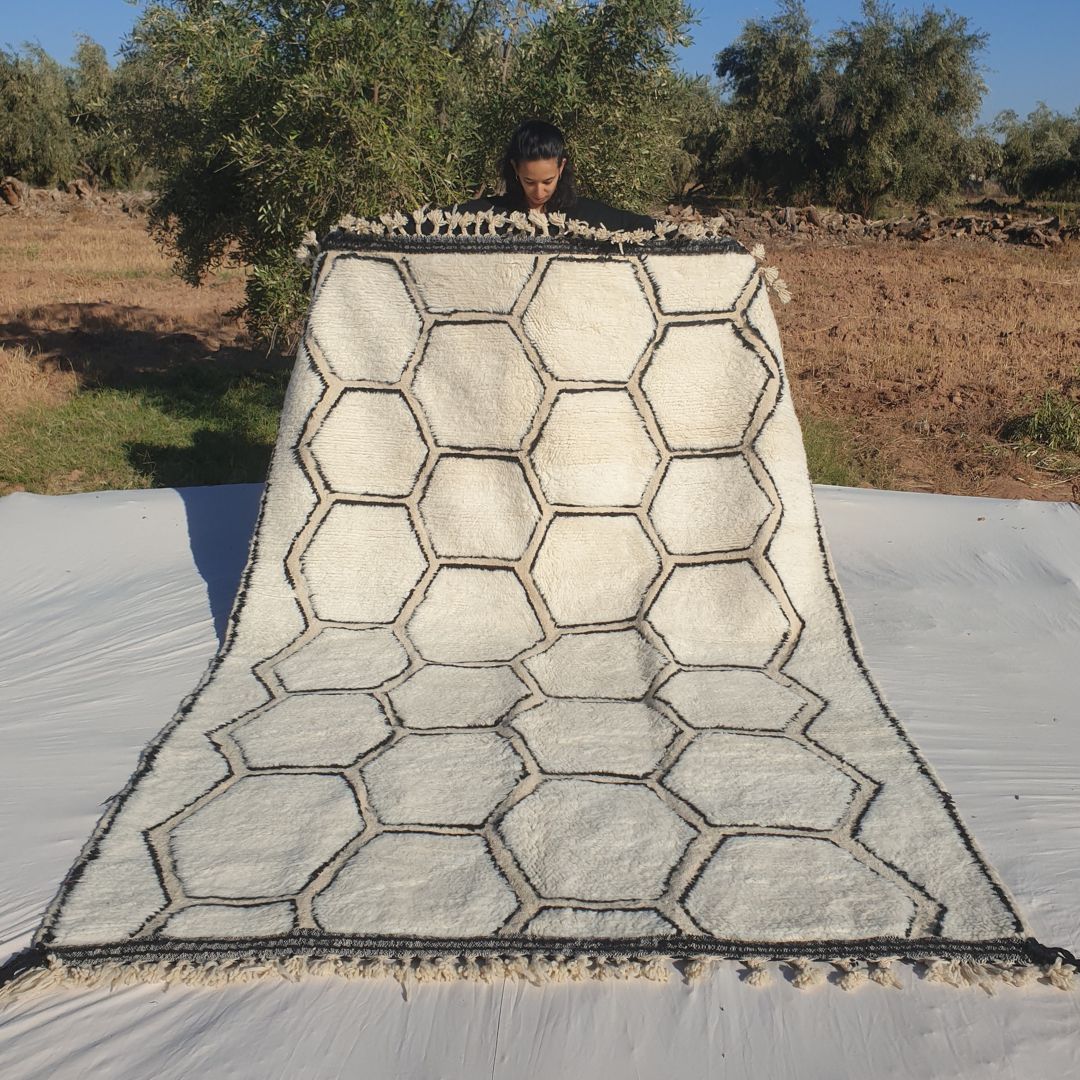 Classic honeycomb geometric 6x9 Beni Ourain Moroccan rug with interconnected hexagons in deep black on soft creamy ivory wool, ultra-fluffy high-pile texture, displayed outdoors in olive grove under blue sky