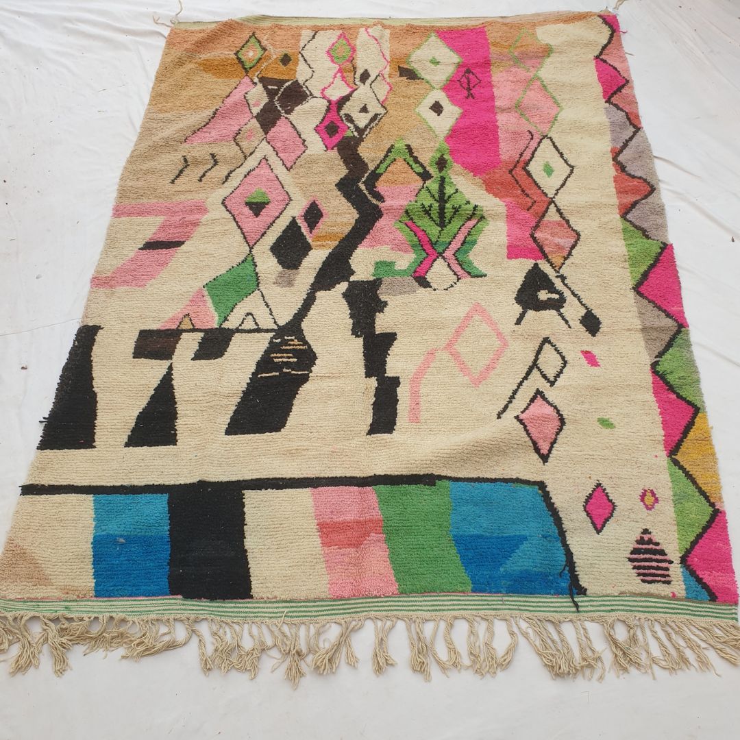 Authentic Boujad Moroccan rug 259×359 cm laid flat — cream background with bold black geometric patterns, fuchsia pink diamond outlines, green botanical leaf motifs and a colorful striped bottom border, handmade in Morocco by Berber women