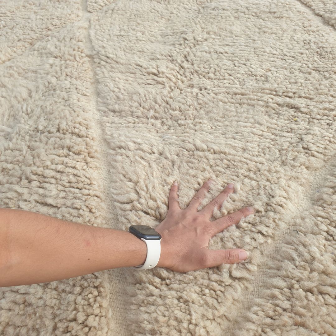 Close-up of a Chaika ivory Beni Ourain rug showing the extraordinary plush depth of the natural wool pile with the classic diamond trellis pattern visible as a carved relief - lighter lines crossing in both directions forming large elongated lozenge shapes, the pattern visible only through shadow and light
