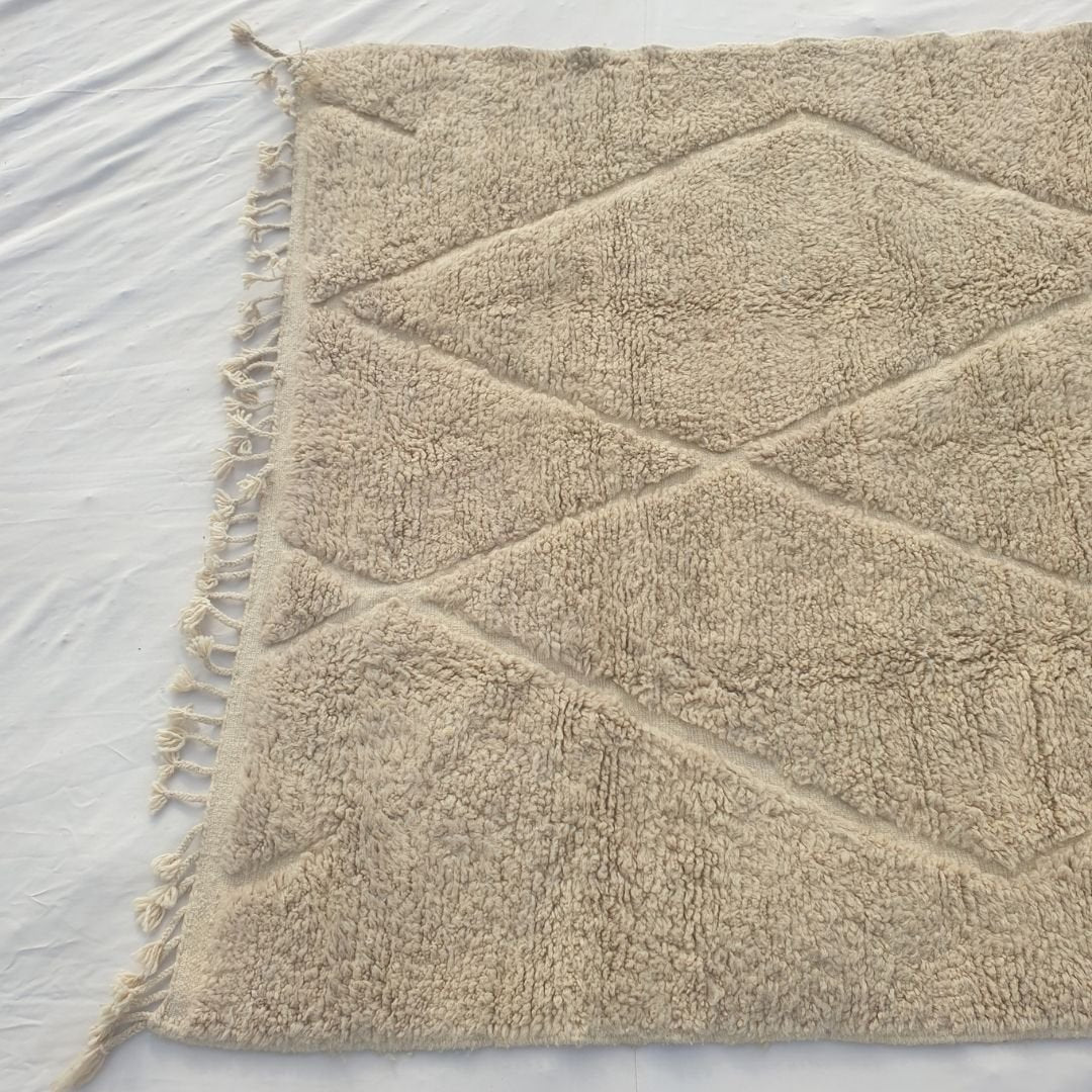 Detail shot of the ivory beige Beni Ourain diamond trellis pattern on Chaika - the carved relief lattice of crossing lines forming overlapping lozenge shapes across the warm ivory wool pile, created entirely without dye through skilled pile height variation, tone-on-tone artistry