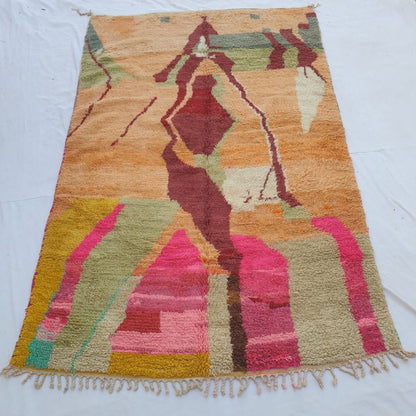handwoven Boujad Berber rug (189x306 cm) laid flat, warm peach-orange ground with a large burgundy abstract silhouette, sage green upper bands, and bold hot pink and olive lower field.