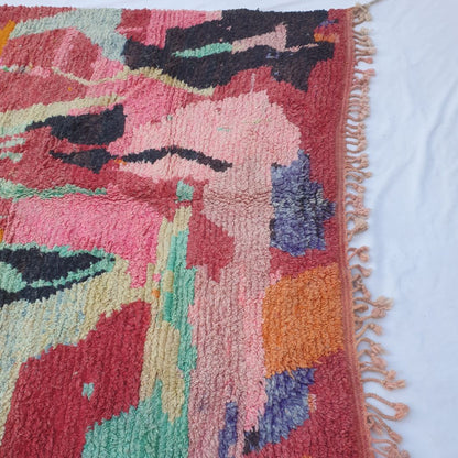 Lower half of Clala Moroccan Berber rug with warm red field, teal pools, purple violet patches and orange accents in dense shaggy handwoven wool with pink-toned fringe.