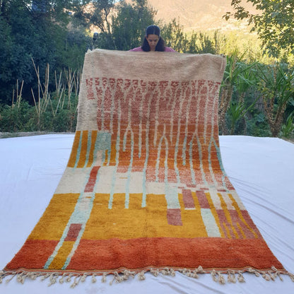 Handwoven 6x10 ft Boujad Moroccan rug with abstract gradient design transitioning from beige to orange and yellow, accented by turquoise and pink geometric elements, perfect for vibrant boho living room or bedroom decor