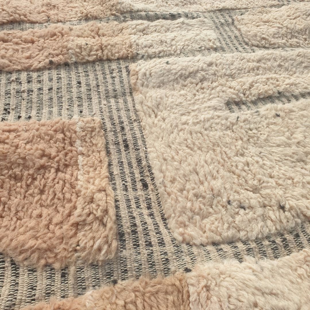 Close-up of a Beni Ourain patchwork rug showing the extraordinary softness of the natural wool pile with large blush-rose and ivory wool blocks side by side, separated by a thin grey grid - an organic, textural two-tone block composition reminiscent of abstract stone or cobblestone