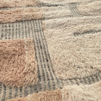Close-up of a Beni Ourain patchwork rug showing the extraordinary softness of the natural wool pile with large blush-rose and ivory wool blocks side by side, separated by a thin grey grid - an organic, textural two-tone block composition reminiscent of abstract stone or cobblestone