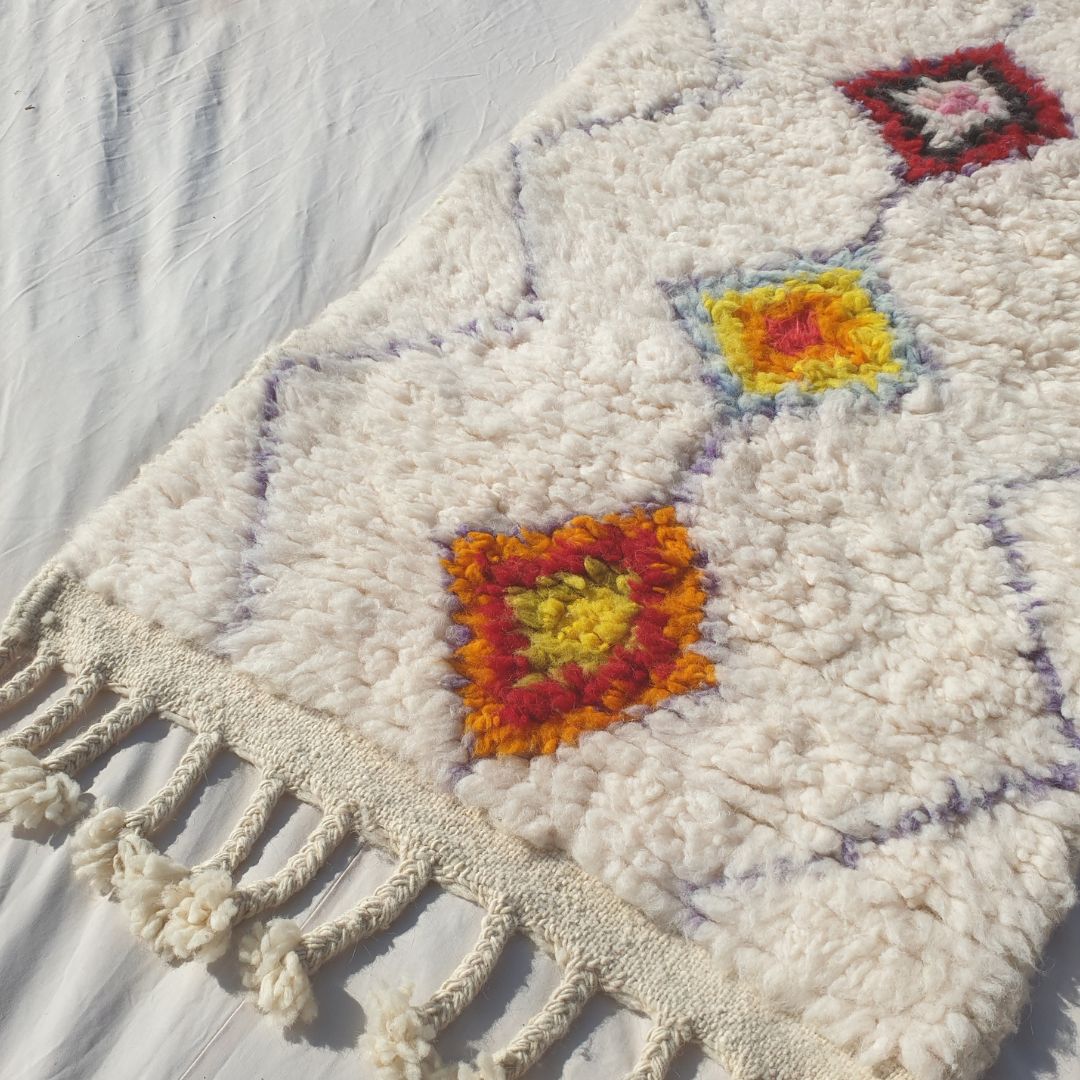 Close-up of a white Beni Ourain runner rug showing the natural ivory wool pile with a fine continuous diamond lattice background and a central column of individual solid-filled diamonds — each diamond a different warm earthy single colour in orange, rust, yellow, wine and mauve, all handwoven in 100% natural Atlas mountain wool
