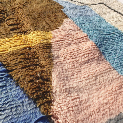 Detailed abstract geometric motifs including central diamond, triangles and color blocks in soft blue, pastel pink, warm beige, brown and yellow on authentic Beni Ourain shag rug
