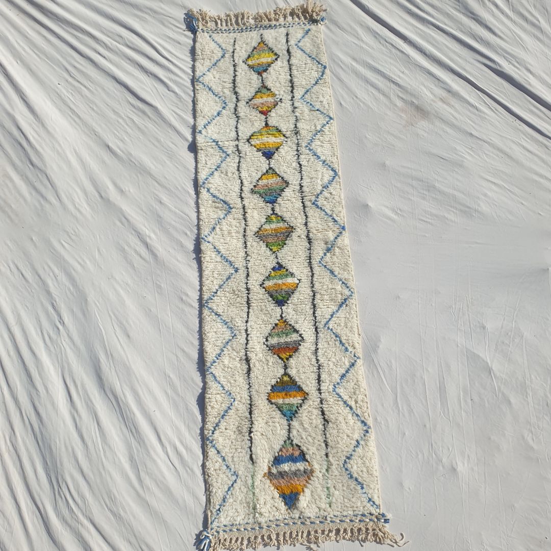 Authentic Beni Ourain Moroccan runner rug 75×282 cm laid flat — white cream natural wool base with a central column of multicolor striped diamonds running its full length, each diamond individually coloured in unique stripe combinations, parallel black flanking lines and a blue zigzag border, handwoven in Morocco