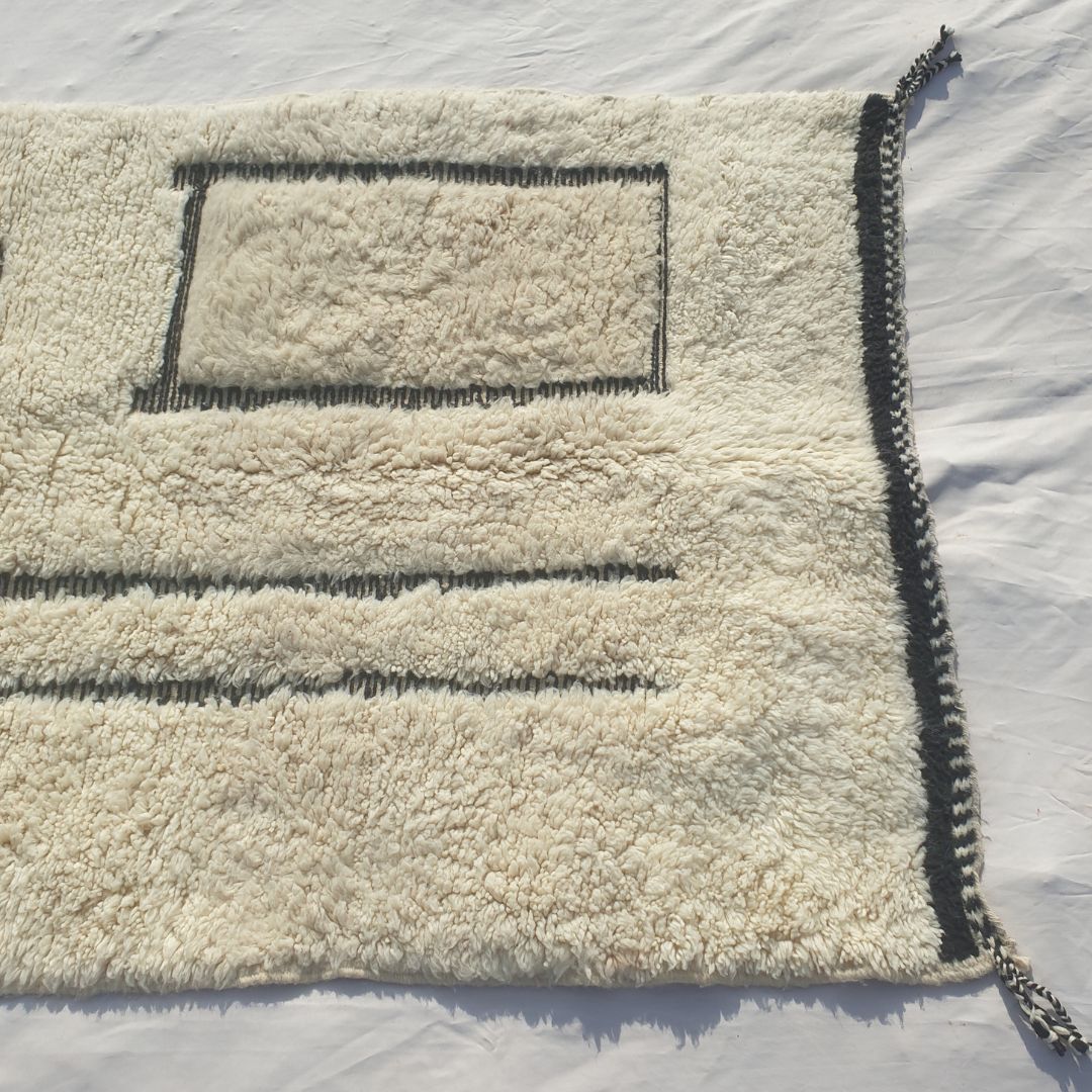 Detail shot of the black line art composition on Kabna Beni Ourain rug - the asymmetric arrangement of two vertical parallel black lines and a black rectangle outline on a pure white ivory wool ground, an abstract minimalist composition of architectural clarity handwoven in Morocco