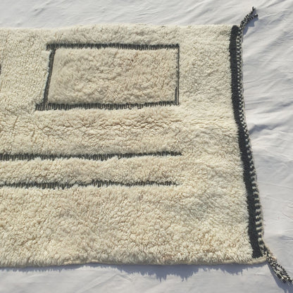 Detail shot of the black line art composition on Kabna Beni Ourain rug - the asymmetric arrangement of two vertical parallel black lines and a black rectangle outline on a pure white ivory wool ground, an abstract minimalist composition of architectural clarity handwoven in Morocco