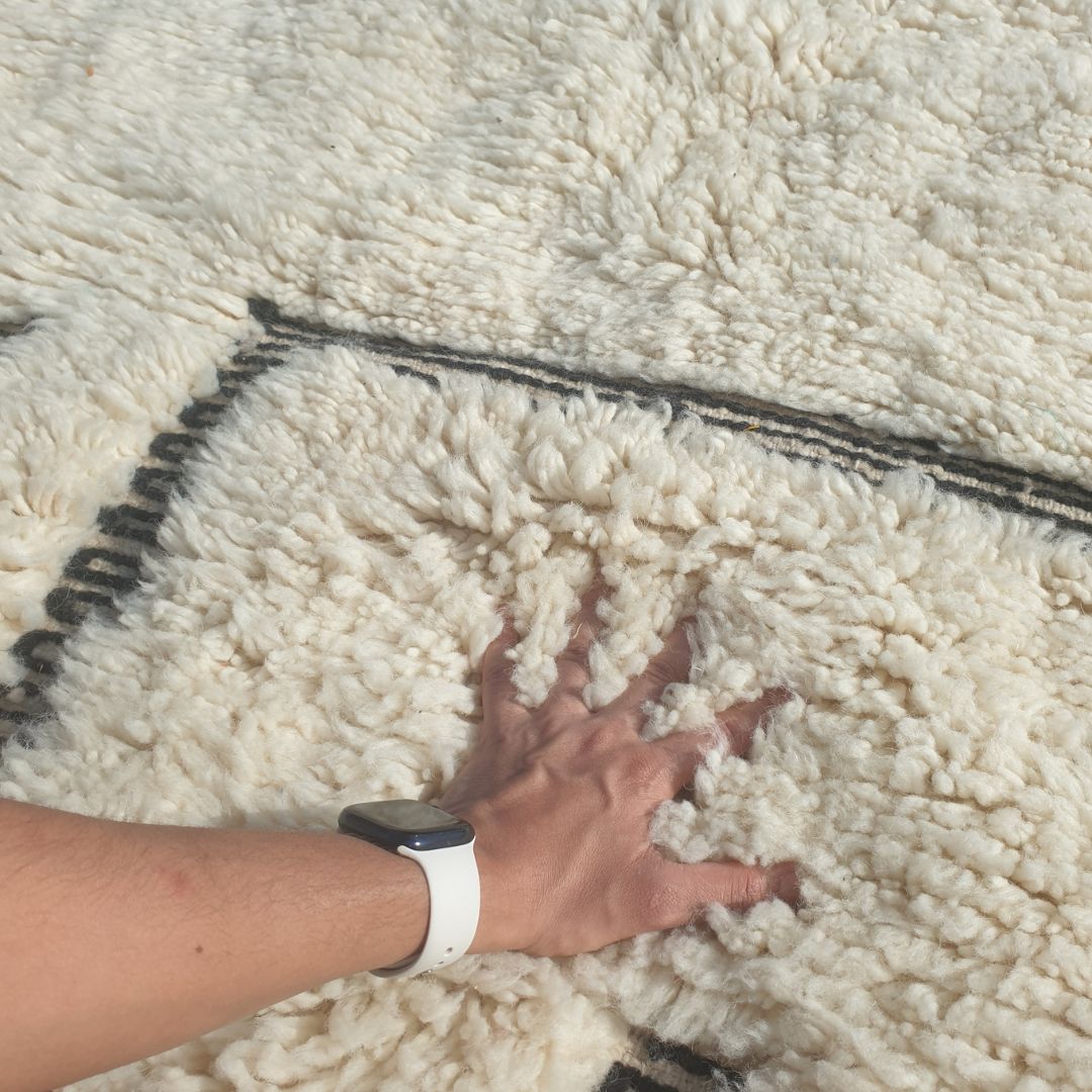 Close-up of a Kabna black and white Beni Ourain rug showing the clean ivory wool pile with bold black line elements - the standalone rectangle outline sitting in the lower portion of the field alongside the vertical parallel lines, the composition reading as an abstract architectural sketch or doorway in natural wool