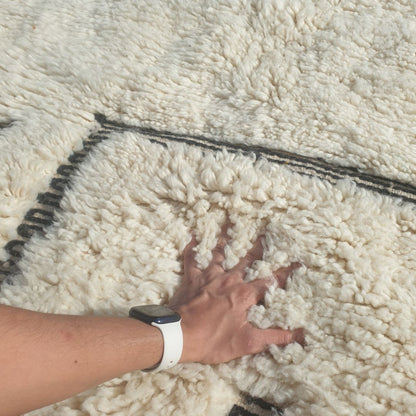 Close-up of a Kabna black and white Beni Ourain rug showing the clean ivory wool pile with bold black line elements - the standalone rectangle outline sitting in the lower portion of the field alongside the vertical parallel lines, the composition reading as an abstract architectural sketch or doorway in natural wool