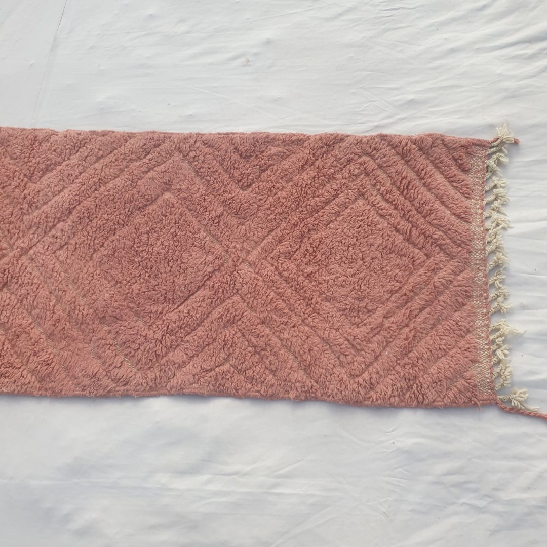 Detail shot of the diagonal carved diamond relief on Karisa terracotta rose Beni Ourain runner - the subtle textured sheen created by pile height variation across the saturated rose-terracotta wool field, a sculptural single-colour composition of remarkable depth