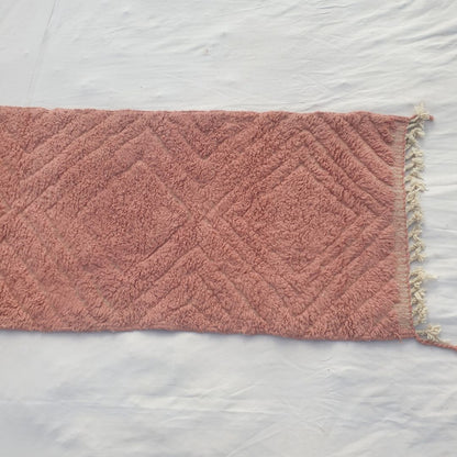 Detail shot of the diagonal carved diamond relief on Karisa terracotta rose Beni Ourain runner - the subtle textured sheen created by pile height variation across the saturated rose-terracotta wool field, a sculptural single-colour composition of remarkable depth