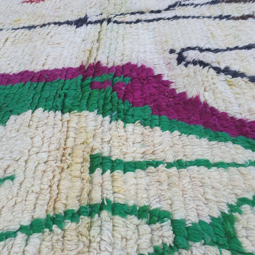 Close-up of Laaqo Boujad Moroccan rug showing the intricate bare black tree branches with fine line work on ivory wool, and vivid magenta angular forms and green outlined diamond shapes on either side.