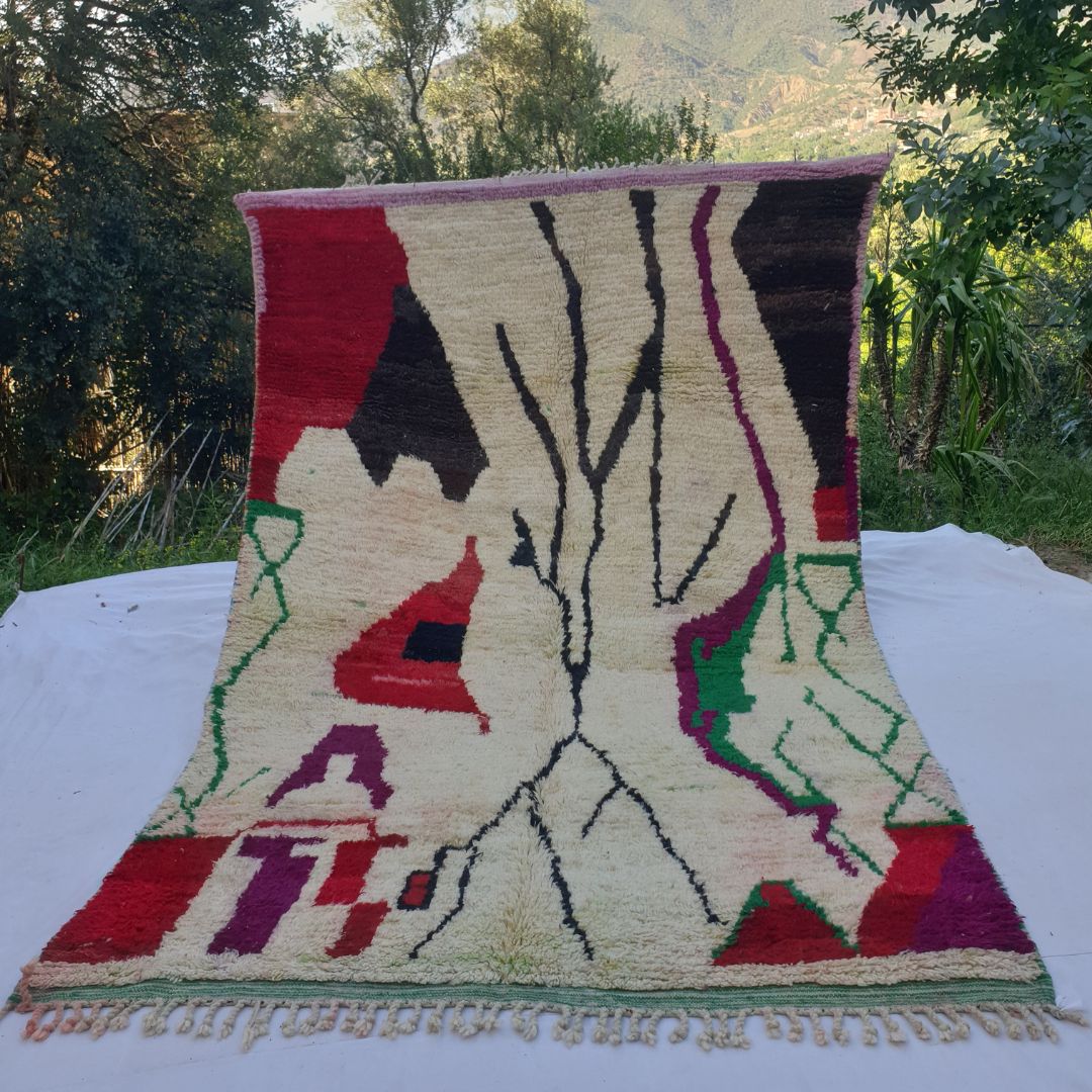 large ivory Boujad Moroccan rug in nature, showing a dramatic bare black tree rising from the centre surrounded by bold red, magenta, brown and green tribal shapes.