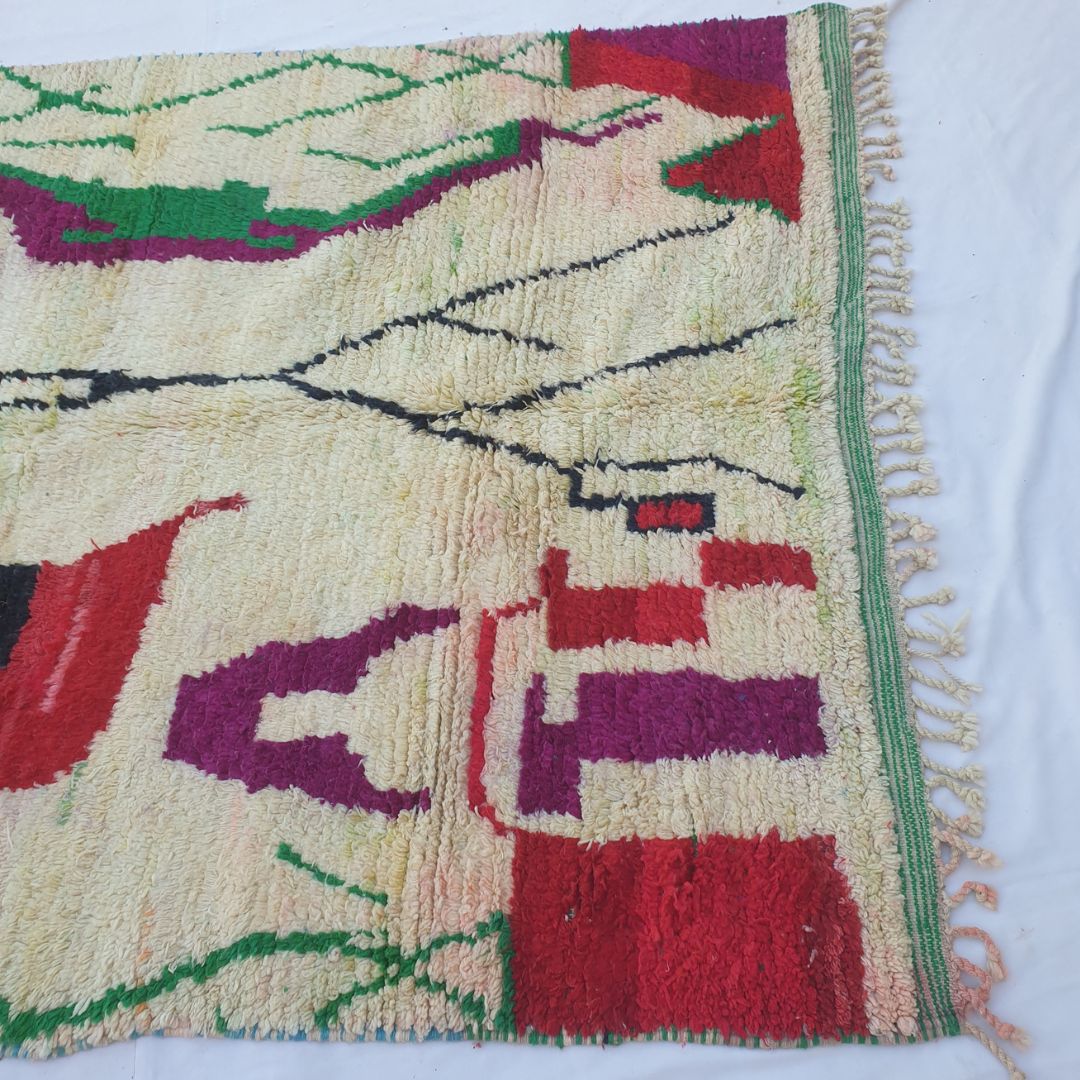 Lower half of Laaqo Moroccan Berber rug with ivory ground, bold red and magenta geometric architectural shapes, small orange and red blocks, and soft green stripe border in thick hand-knotted wool pile.