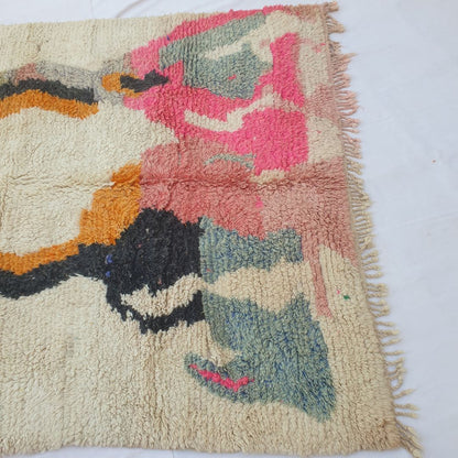 Lower half of Lahca Moroccan Berber rug with large freeform abstract shapes — bold hot pink mass centre-right, slate-blue grey forms on both lower sides, an irregular black blob lower-left, and golden-yellow centre accent — on an open ivory field in dense hand-knotted wool with pink-toned fringe.