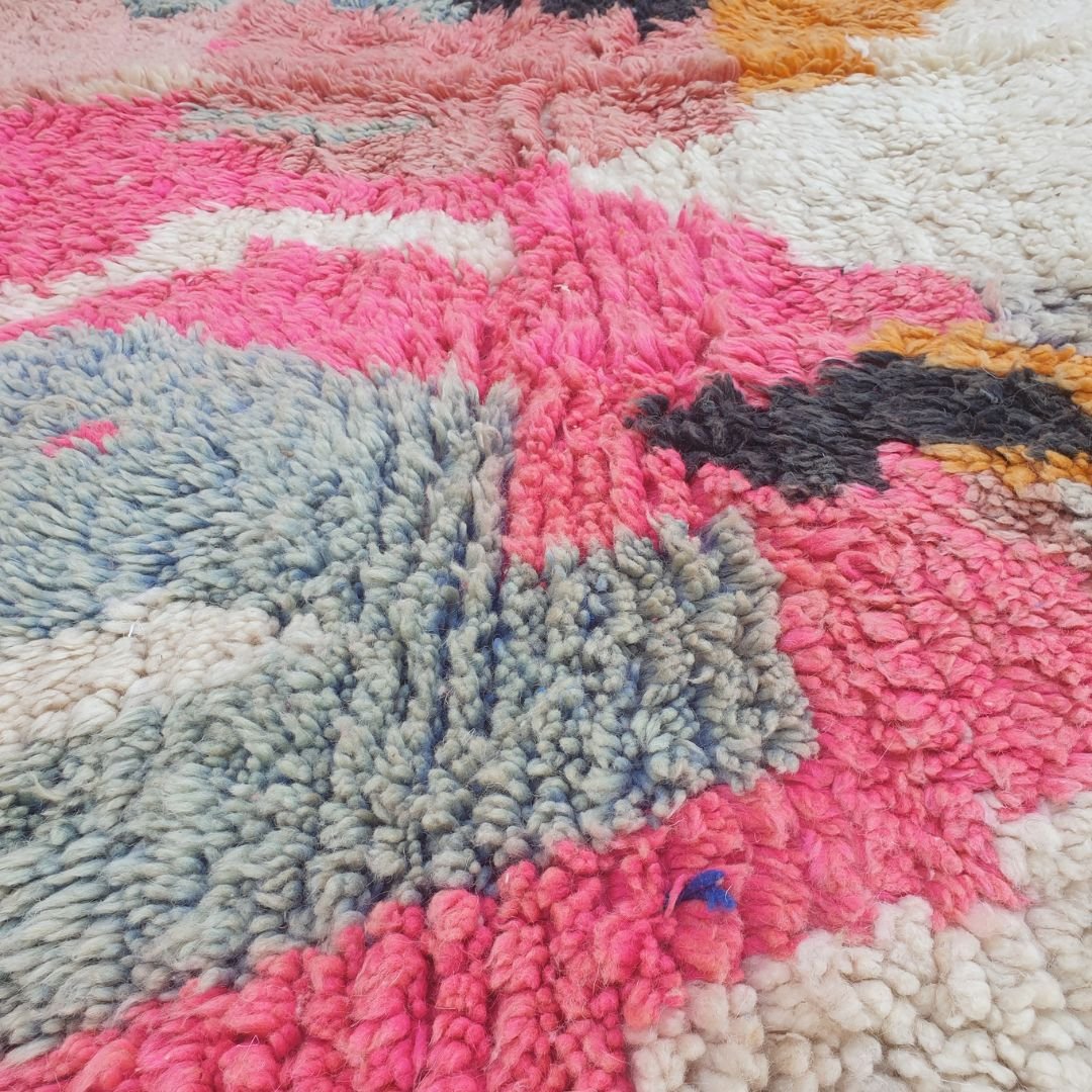 Close-up of Lahca Boujad Moroccan rug upper section showing the bold orange and dark charcoal grey zigzag lightning columns with soft grey and blush-pink triangular accents descending against the thick ivory wool ground.