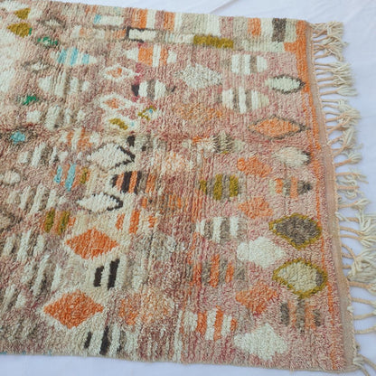 Lower half of Lahnac Moroccan Azilal rug with warm terracotta-pink ground, scattered ivory cream ovals, mustard gold diamonds, orange accents and dark brown details in thick, soft hand-knotted wool pile with cream fringe.