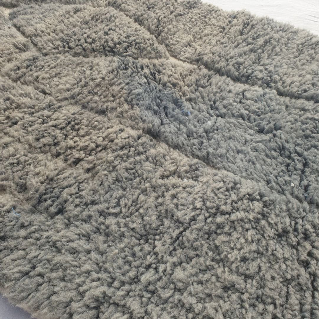 Close-up of a Minayta grey taupe Beni Ourain accent rug showing the soft natural wool pile with the dark architectural line composition - the stepped vertical frame and the diamond accent visible against the muted green field, a small-scale abstract composition handwoven in 100% natural wool