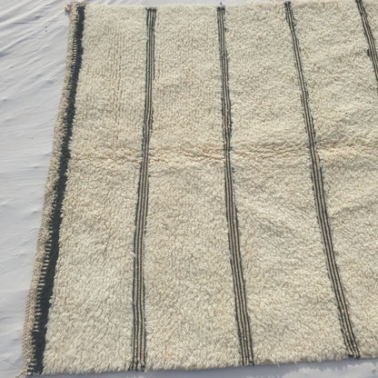Bottom half of an ivory Beni Ourain Moroccan rug showing the black-and-white checkered border and the final black stripe clusters against the natural wool pile, with hand-knotted fringe - the exceptional softness of authentic Beni Ourain wool