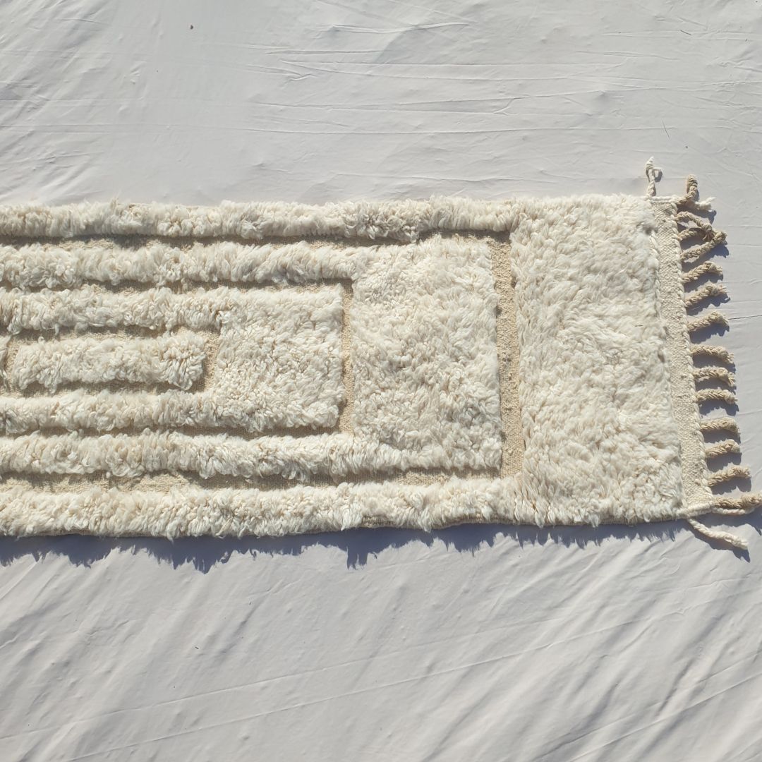 Bottom half of a pure white Beni Ourain Moroccan runner showing the natural undyed ivory wool pile and the delicate carved concentric rectangle pattern visible in the pile texture, with the natural knotted fringe — the softness and warmth of authentic High Atlas Beni Ourain wool