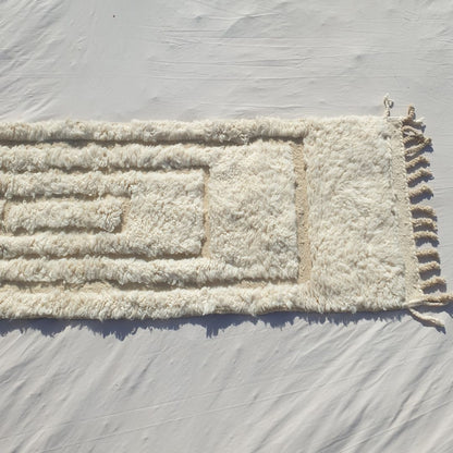 Bottom half of a pure white Beni Ourain Moroccan runner showing the natural undyed ivory wool pile and the delicate carved concentric rectangle pattern visible in the pile texture, with the natural knotted fringe — the softness and warmth of authentic High Atlas Beni Ourain wool