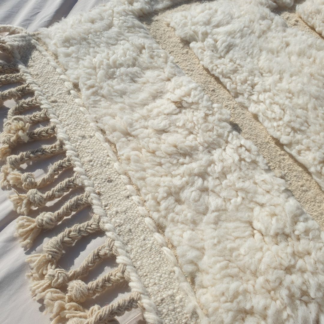 Close-up of a white Beni Ourain runner rug showing the extraordinary softness of the natural ivory wool pile with a subtle carved geometric relief pattern — nested rectangular frames created through pile height variation rather than colour, an incredibly tactile and sophisticated Moroccan hallway rug