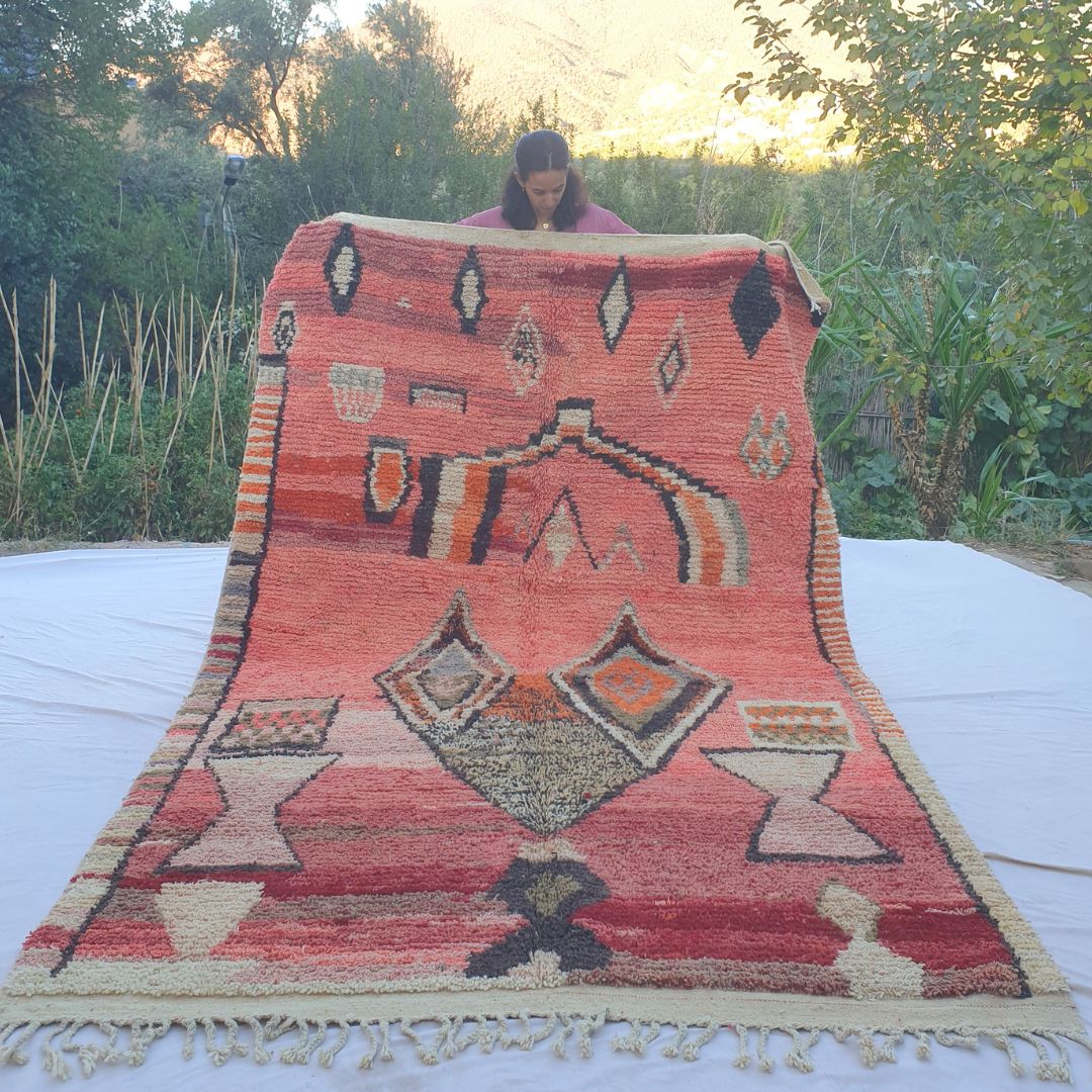 Large 6x10 vibrant coral red Boujad Moroccan rug with bold black, orange and cream Berber symbols held outdoors at sunset
