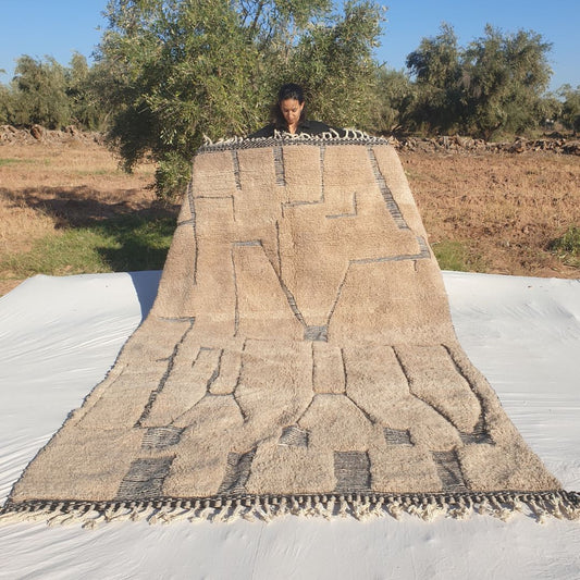 Large 7x11 abstract Beni Ourain Moroccan rug featuring bold black geometric shapes, irregular rectangles, tribal lines and asymmetrical motifs on creamy ivory wool, ultra-fluffy high-pile texture, displayed outdoors in olive grove