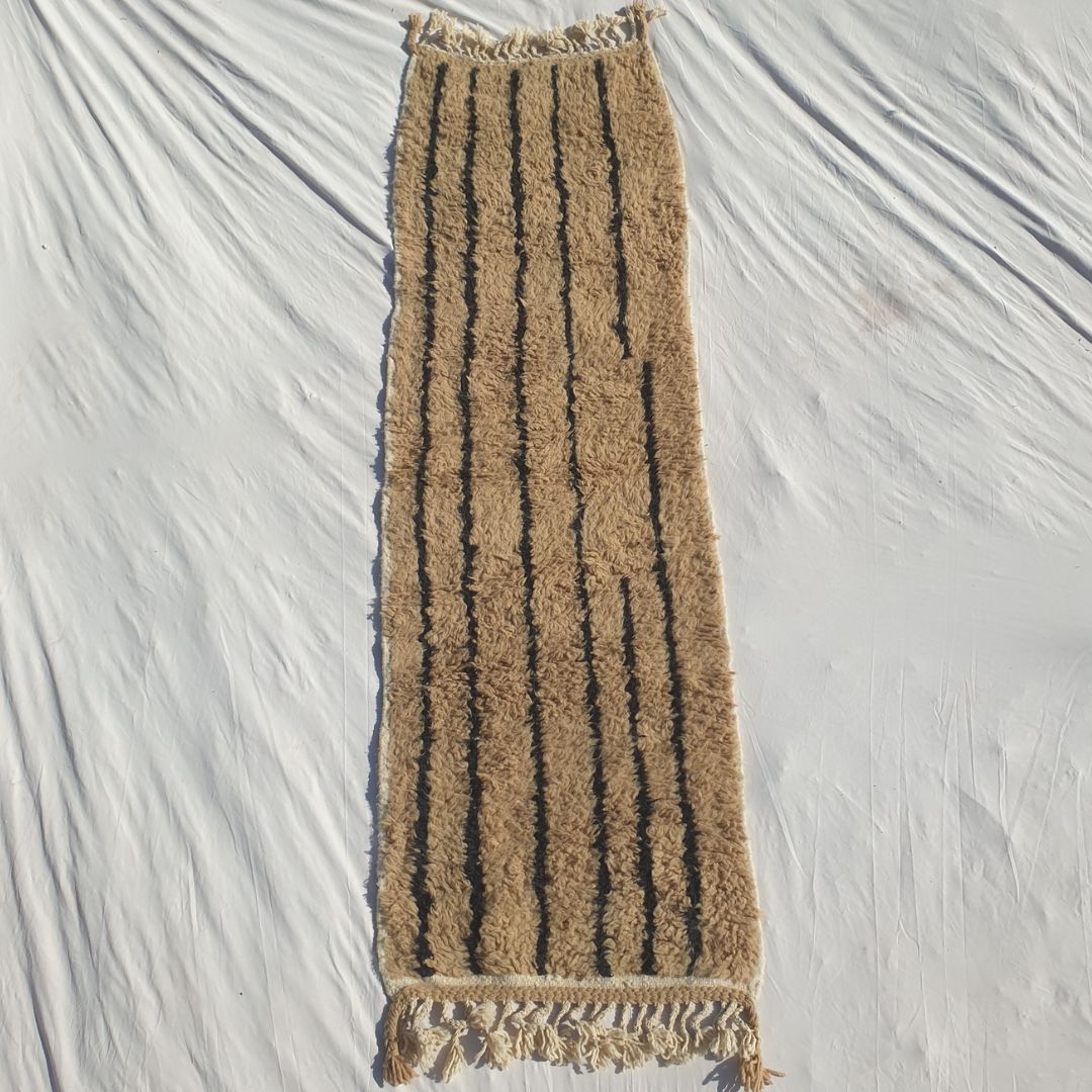 Authentic Beni Ourain Moroccan runner rug 85x280 cm laid flat - warm natural camel and beige undyed wool base with clean vertical black stripe lines running the full length, a beautifully minimal and architecturally refined composition, handwoven in Morocco by Beni Ourain Berber women