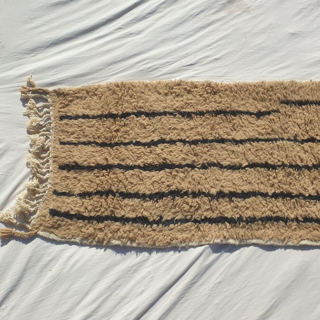 Bottom half of a warm beige Beni Ourain Moroccan runner showing the natural camel wool pile with the clean vertical black stripe pattern running to the end, with natural knotted fringe - the warmth and softness of authentic Beni Ourain High Atlas wool in a calming natural palette