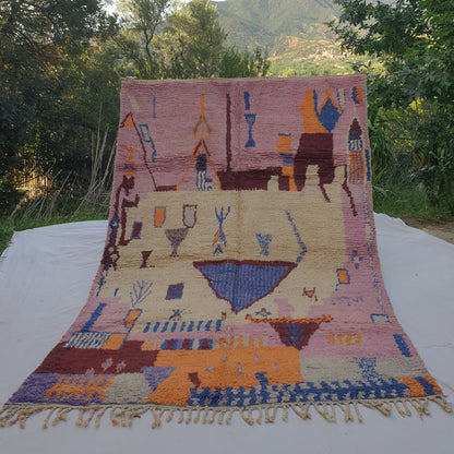 large pink and ivory Boujad Moroccan rug held up in nature, revealing a striking blue triangle centrepiece surrounded by rare figurative symbols in cobalt and orange.