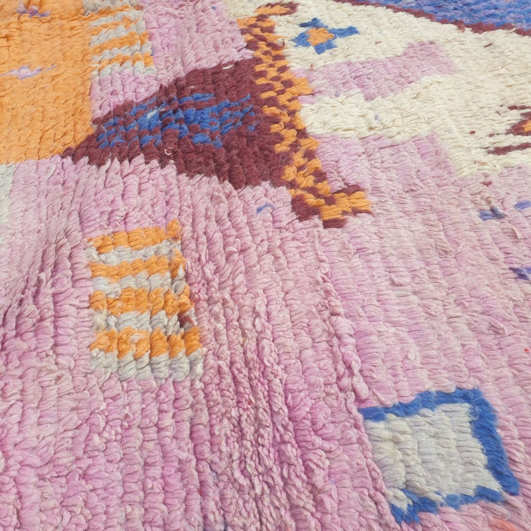 Close-up of Tescla Boujad Moroccan rug showing rare figurative motifs — goblet shapes, human stick figures with raised arms, tree branches — in cobalt blue and orange on an ivory wool field.