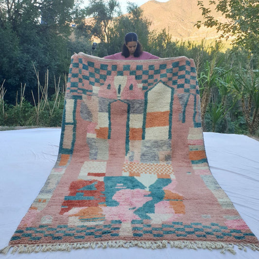 Vibrant handwoven 6x10 Boujad Moroccan rug featuring abstract geometric patterns in pastel pinks, reds, greens, and blues, displayed outdoors against a mountainous backdrop.