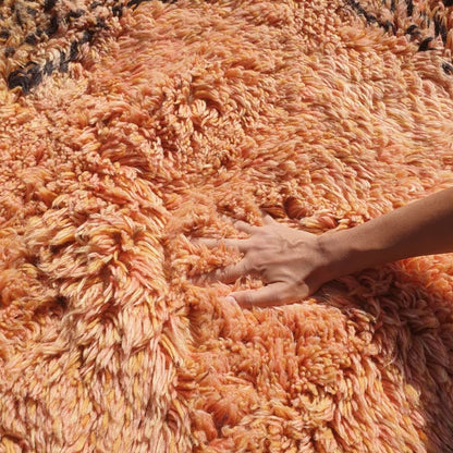 Close-up of a feminine hand pressing into the ultra-soft thick pile of a Beni Mrirt Moroccan rug, showing the deep terracotta wool fibers flowing between fingers