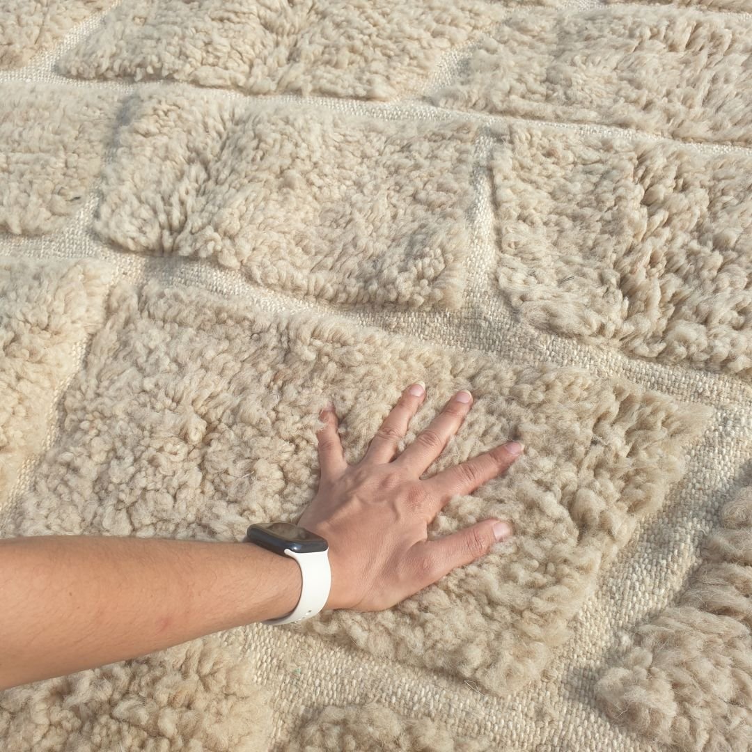 Close-up of a Yabre ivory Beni Ourain rug showing the extraordinarily plush natural wool pile with a carved brick relief pattern - irregular rectangular blocks of varying widths in horizontal rows, separated by thin recessed lines creating a cobblestone or stone wall effect, entirely without dye, created through pile height variation